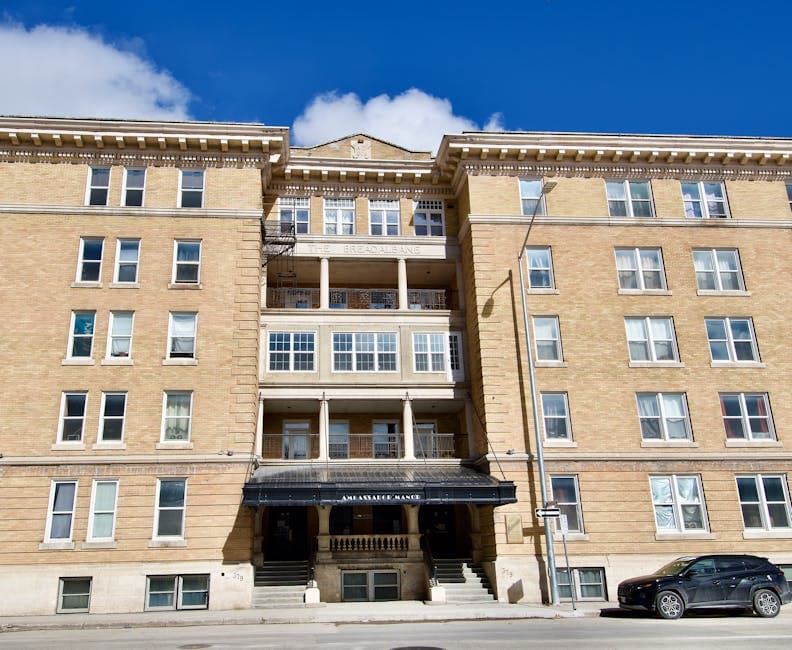 Historic Winnipeg apartment building facade on a sunny day with overgrown weeds along the exterior