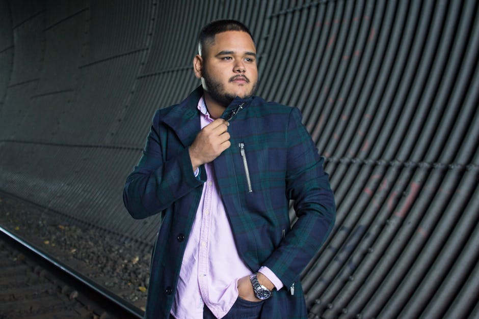 Fashionable man posing confidently in a tunnel, showcasing modern style with a checkered jacket.
