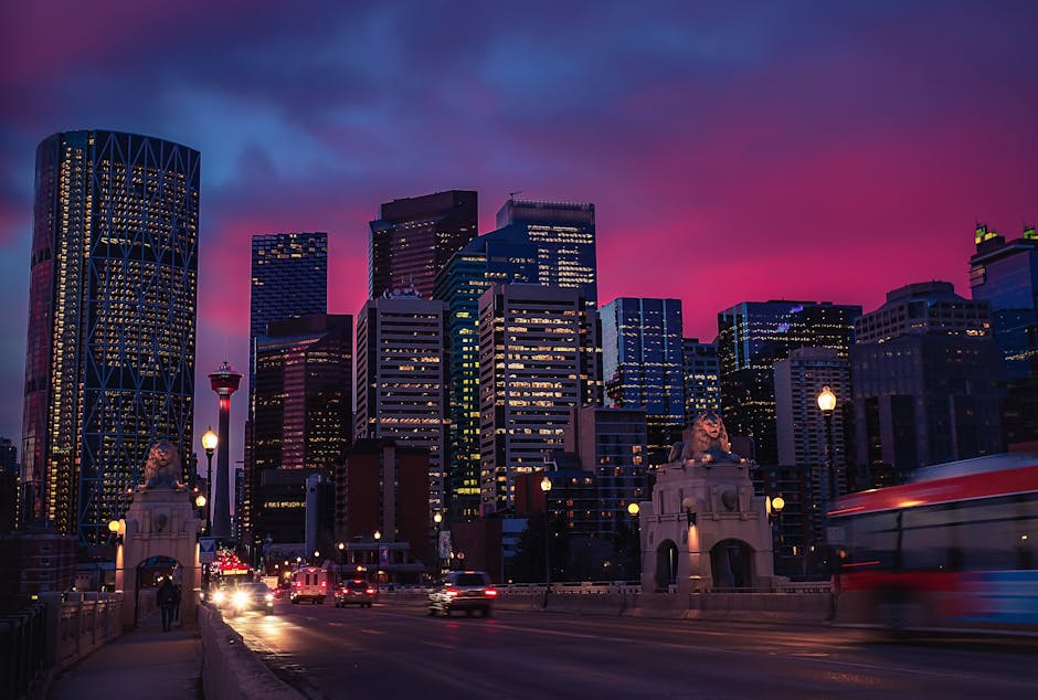Stunning view of Calgary's illuminated skyline during a vibrant pink sunset, featuring skyscrapers and urban landscape.