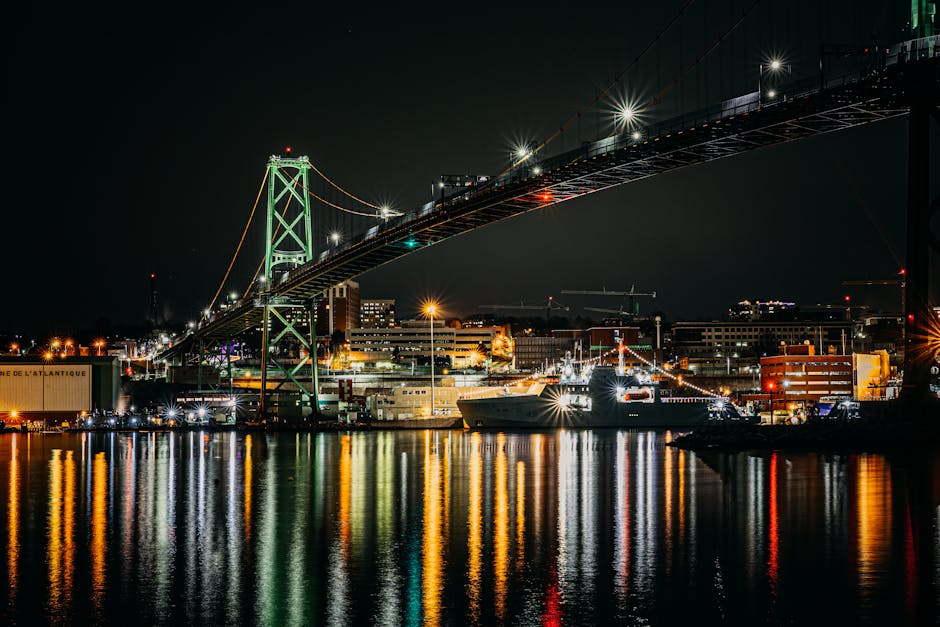 Night view of Halifax harbor featuring a bright suspension bridge with city lights reflecting on water.