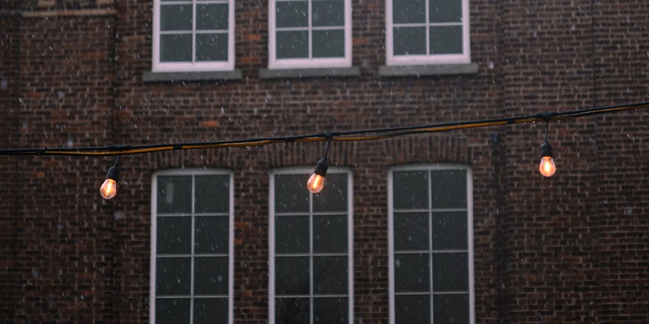 Hanging string lights in front of brick building during snowfall, Longueuil, Quebec.
