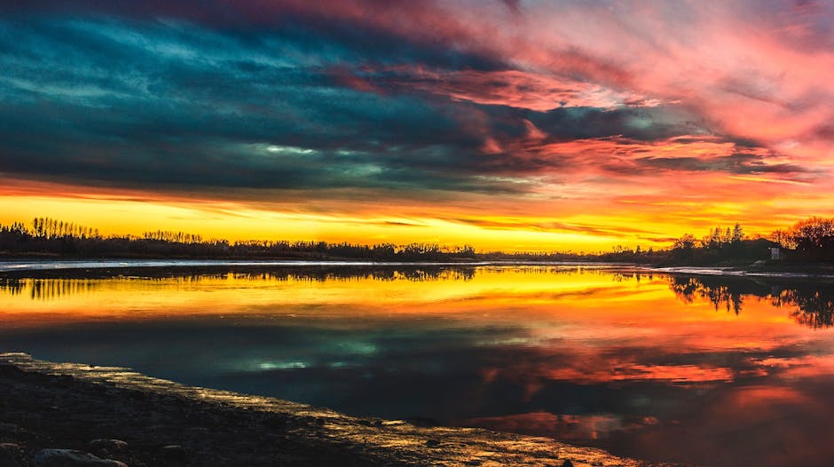 Vibrant sunset over a tranquil lake in Gimli, Canada, capturing the dramatic sky and reflections.