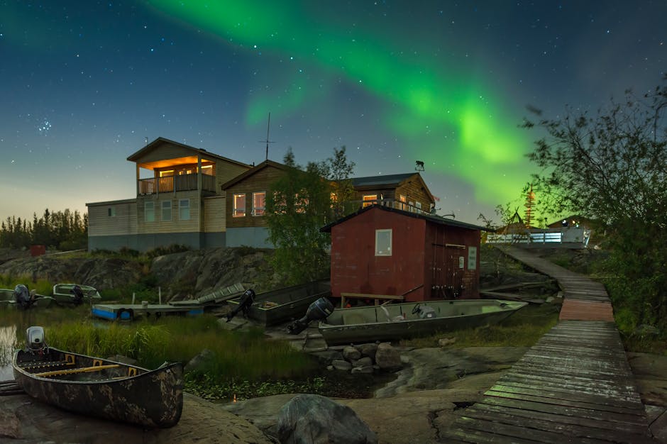 Colorful aurora borealis over rustic lakeside cabins and boats in Yellowknife, Canada.
