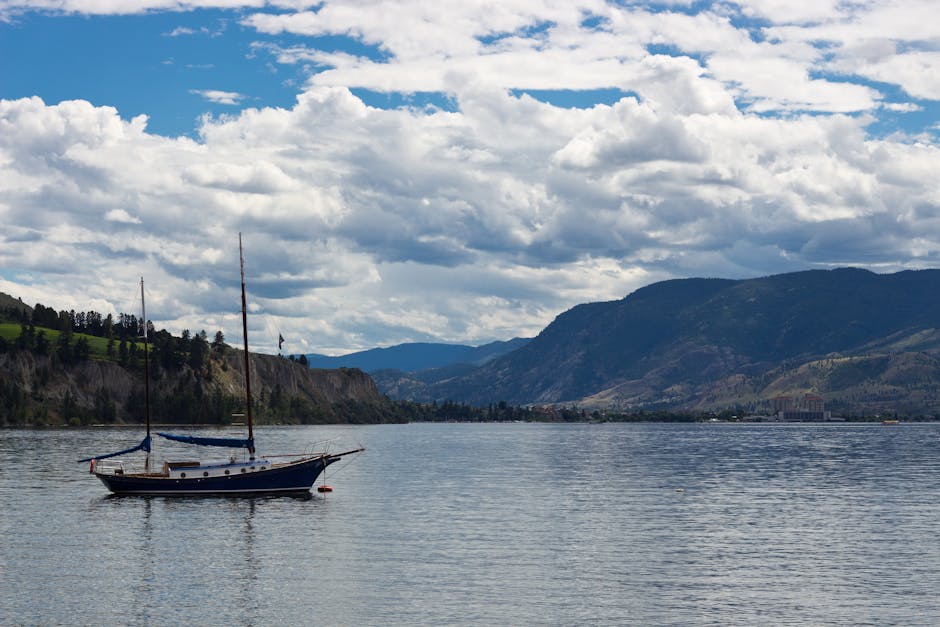 Peaceful scene with a boat on Okanagan Lake, surrounded by mountains and clouds in Kelowna, BC.