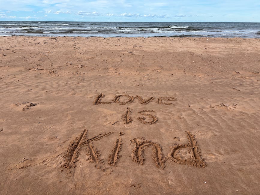 "Love is Kind" written on a beach at Stanhope, conveying positivity and warmth.